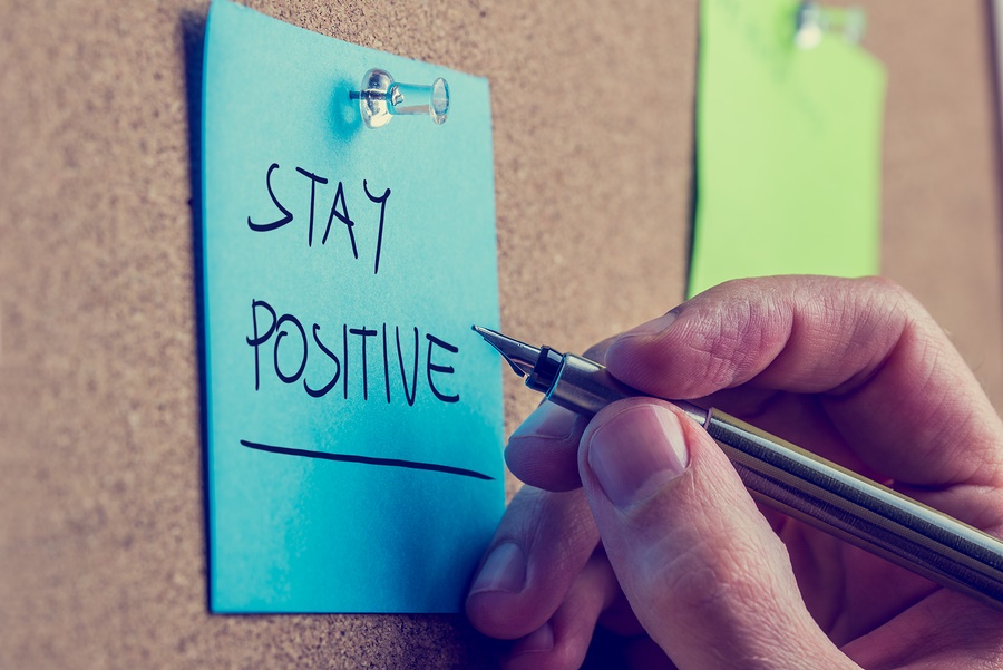 Retro instagram style image of a male hand writing Stay positive on blue post it paper pinned on cork bulletin board.